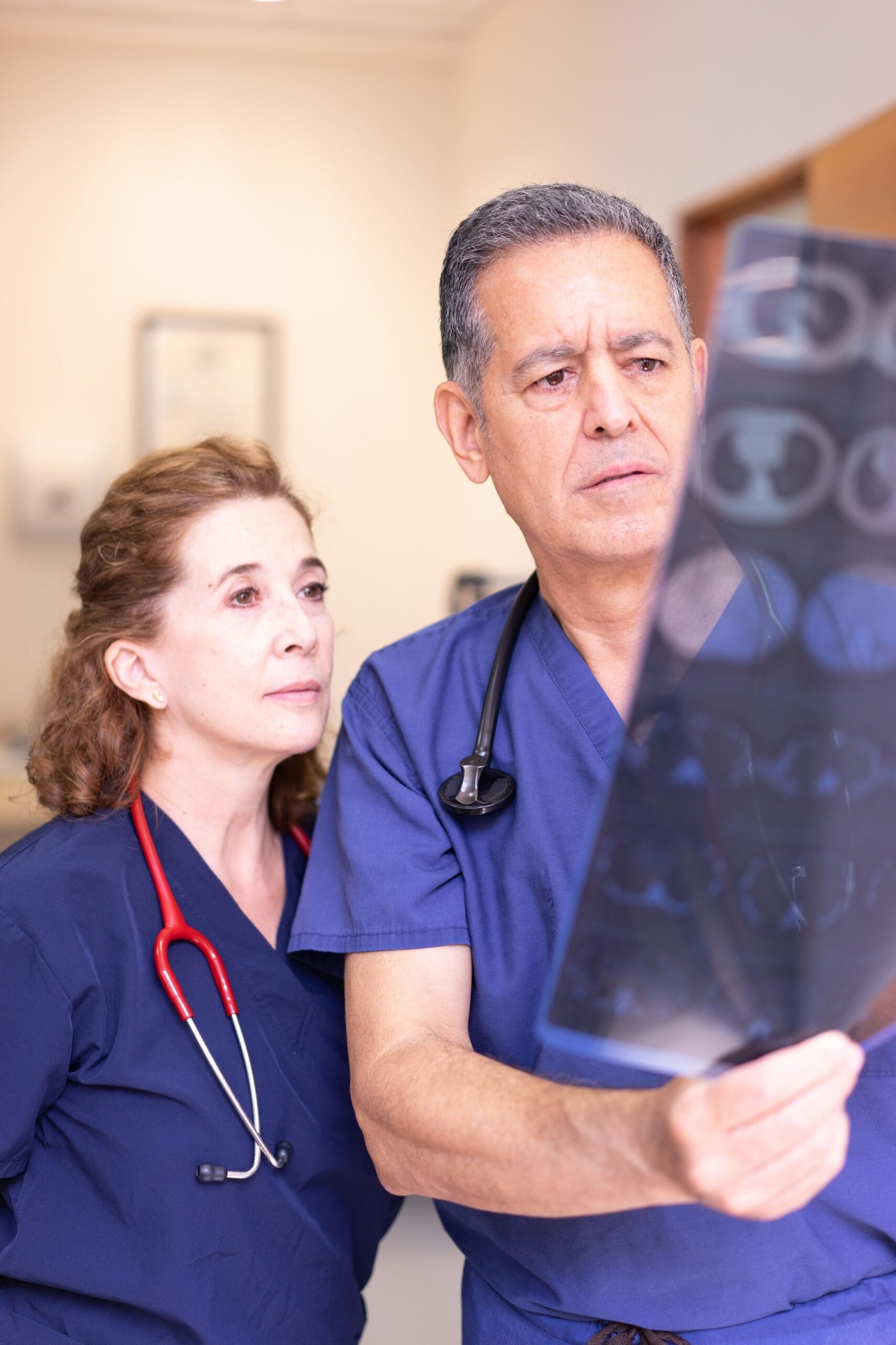 Two healthcare professionals in scrubs examine an x-ray image in a hospital setting.