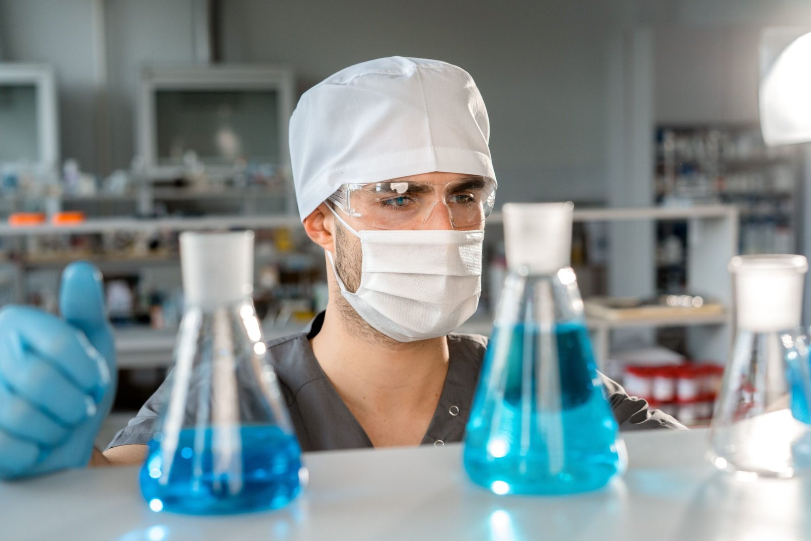 Male scientist in a laboratory analyzing blue chemicals in Erlenmeyer flasks.